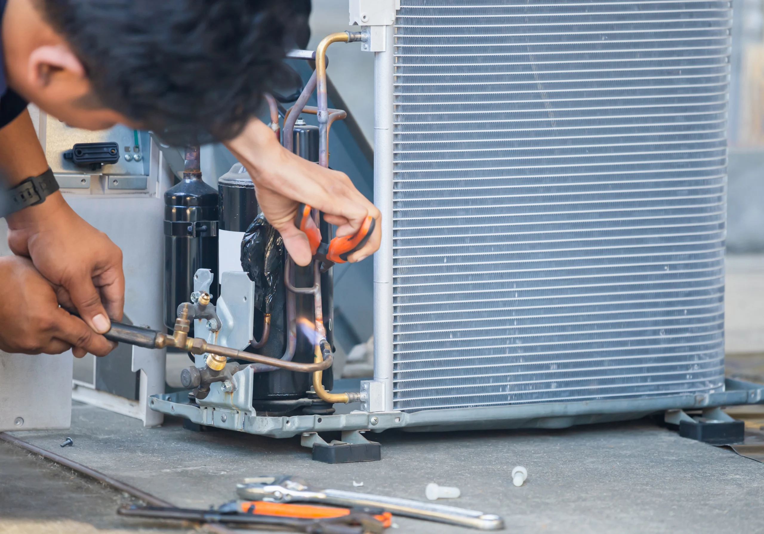 An HVAC technician fixing an air conditioner, using tools to repair the unit. Soldering copper tubing.