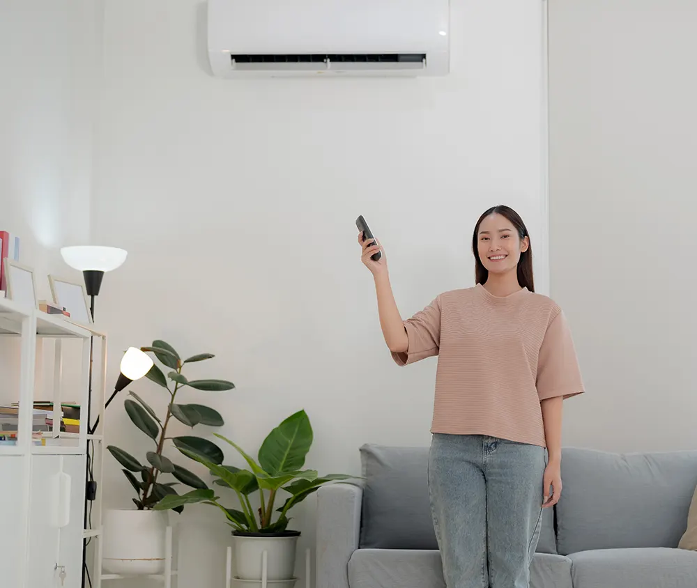 Woman using a remote control to turn on an air conditioner in a modern living room.